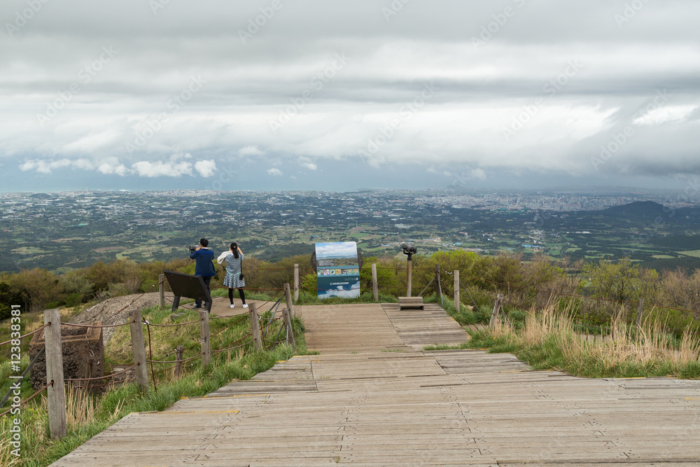 A couple at a vantage point at the Eoseungsangak Peak at the Hallasan National Park watching the view of Jeju Island in South Korea on a cloudy day.