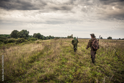 Hunters going through rural field with dramatic sky during hunting season