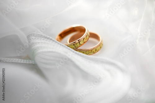 Engagement wedding rings of the bride and groom on a background of delicate white fabric wedding veils. Wedding accessories for the newlyweds.