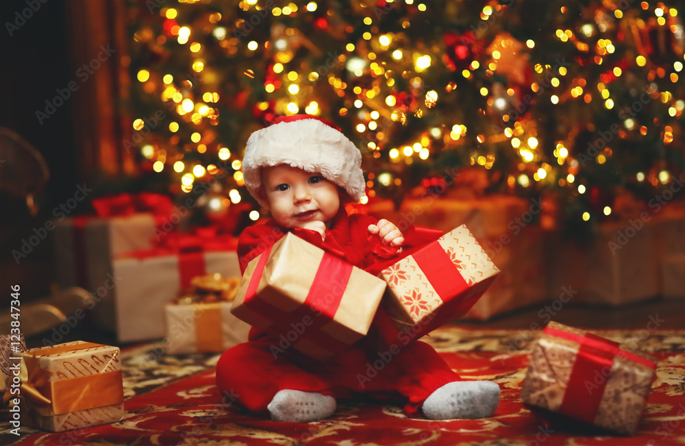 Happy baby by Christmas tree with gifts