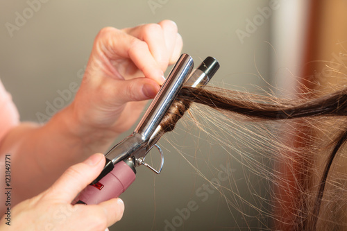 Stylist curling hair for young woman.
