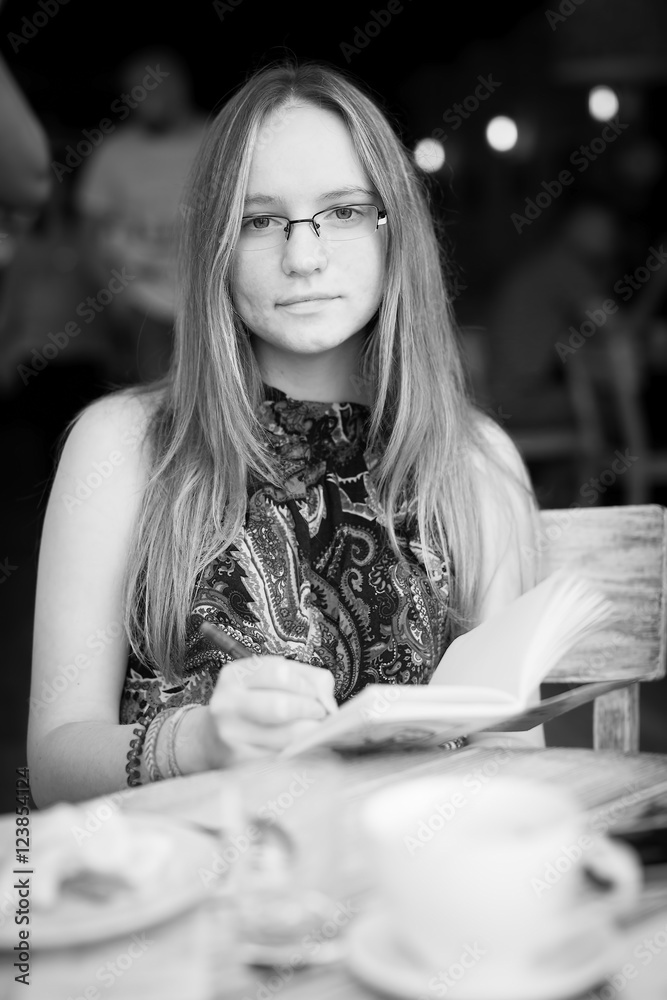 Black and white portrait of a young girl in glasses sitting in a cafe. Black and white portrait of a young girl in glasses sitting in a cafe.