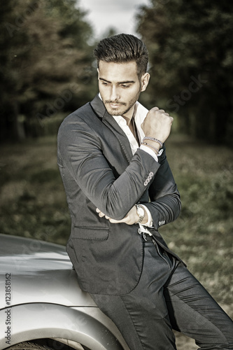 Portrait of young attractiave man in business suit sitting in his new stylish car outdoor in countryside
