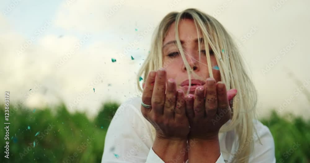 Beautiful young woman blowing glitter into the wind at sunset