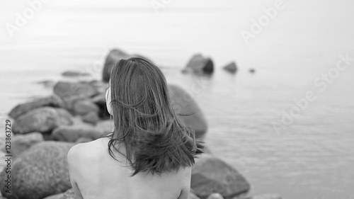 Young woman sitting on stone facing the sea photo