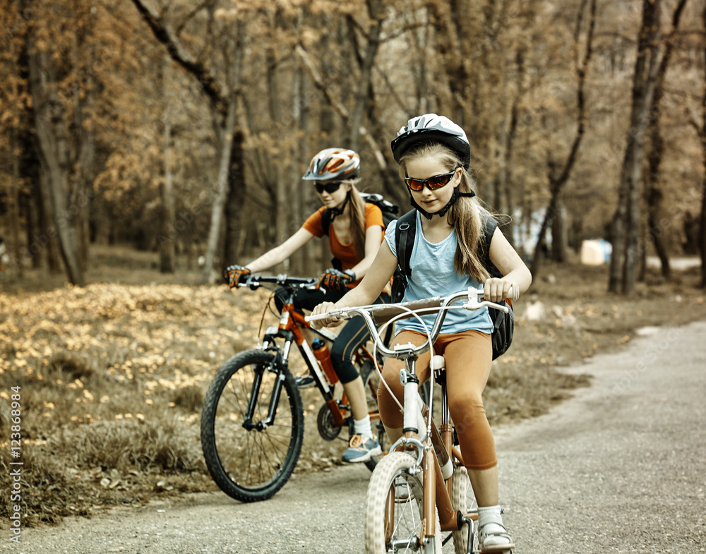 Bikes bicyclist girl. Toned sepia image. Girls wearing bicycle helmet with rucksack ciclyng bicycle. Child in foreground teenager on background.