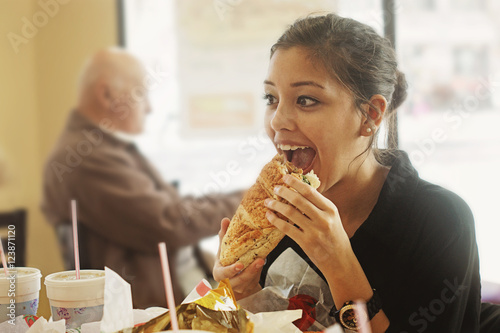 Teenage girl in store eating a  large sandwich