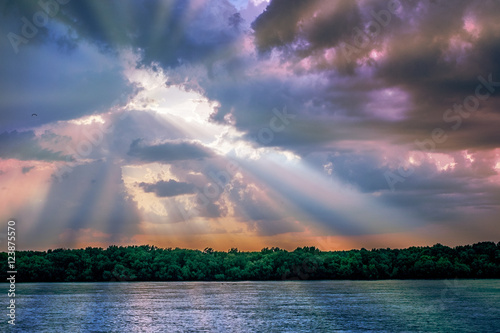 Fotografie Sun rays light through down from rain clouds and reflected in water