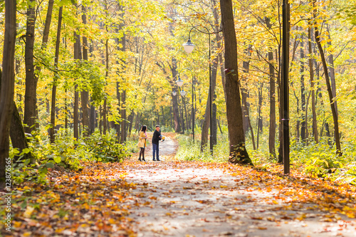 Happy young family walking down the road outside in autumn nature.
