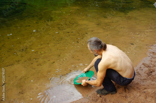 man, prospector panning gold in a river with sluice box