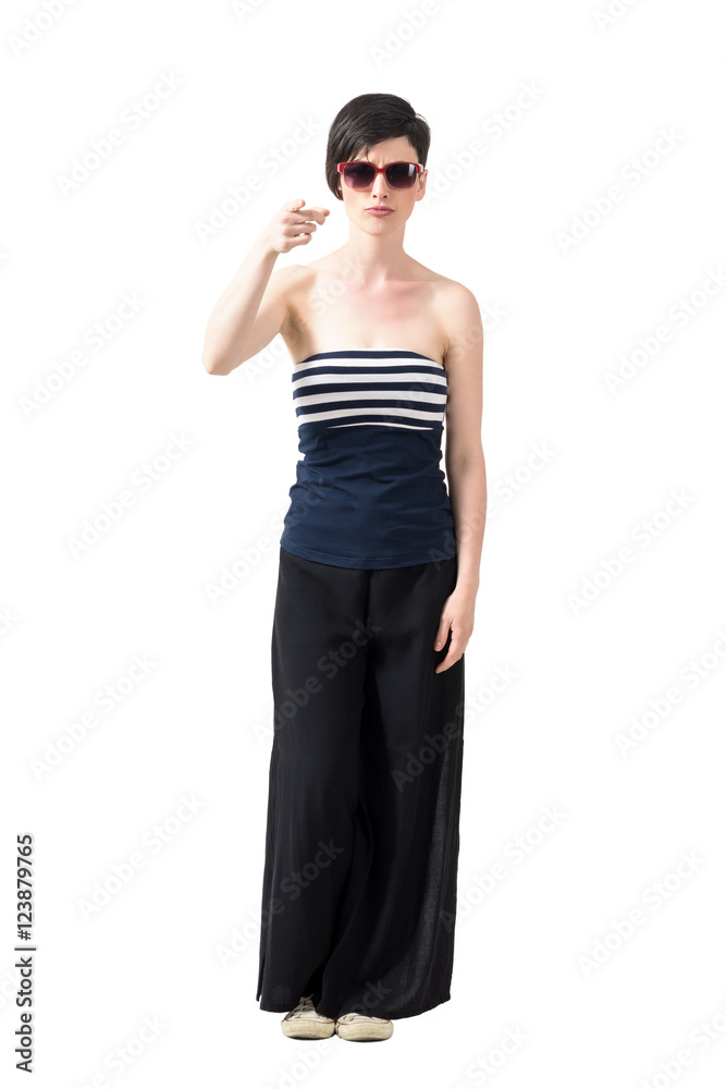 Young trendy short hair woman wearing sunglasses pointing finger at camera. Full body length portrait isolated over white studio background. Young trendy short hair woman wearing sunglasses pointing finger at camera. Full body length portrait isolated over white studio background.