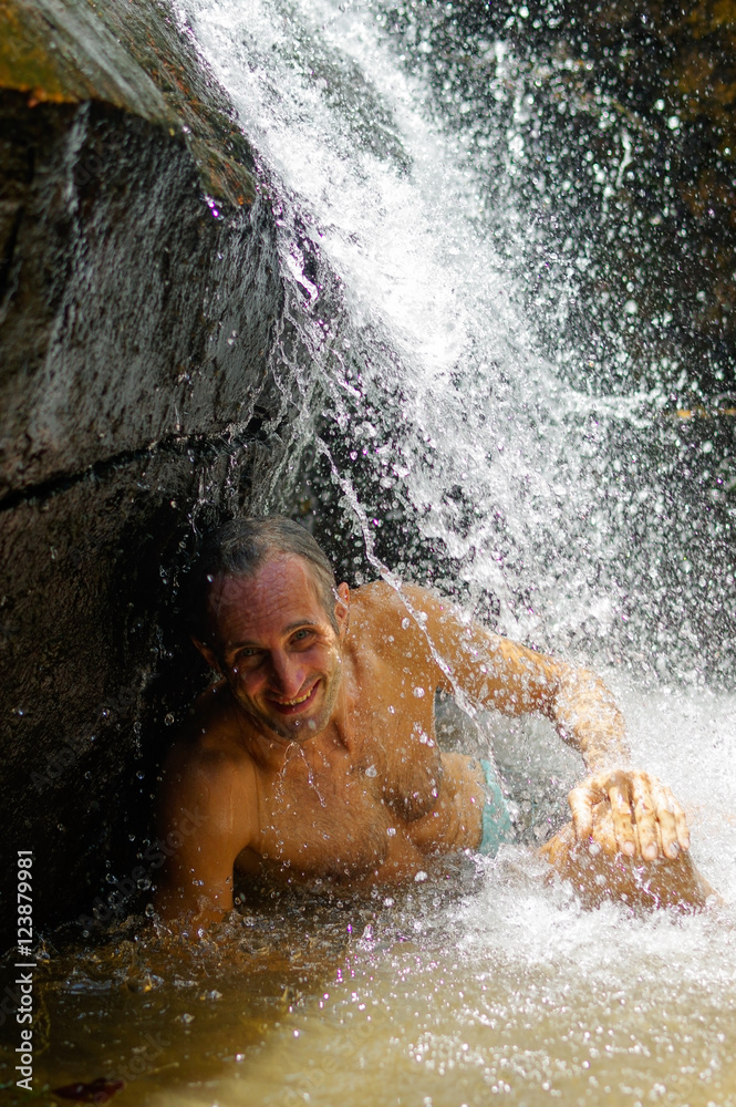 Fototapeta premium Man taking a relaxing shower under waterfall. outside