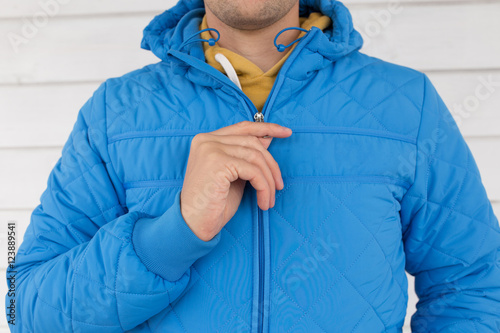 man buttons blue quilted jacket. cropped image of a man's hand fastens with a zipper on the jacket on a white background. close up
