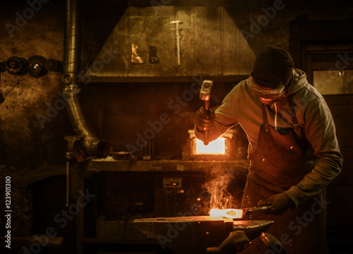 Blacksmith with brush handles the molten metal on the anvil in smithy