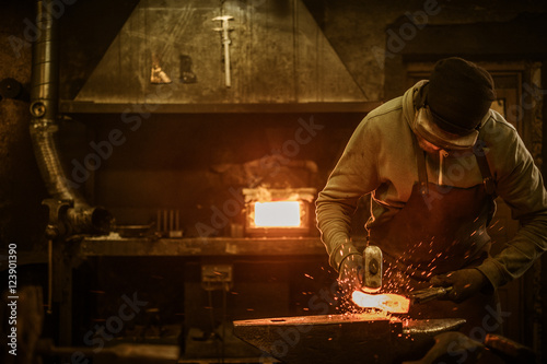 Blacksmith with brush handles the molten metal on the anvil in smithy
