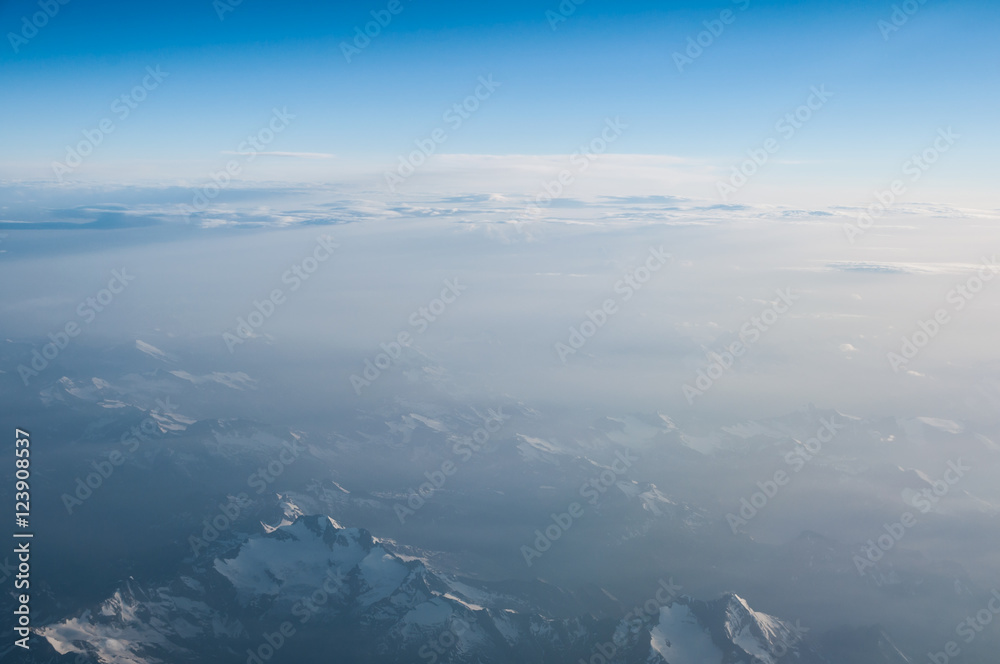 Aerial view from airplane flying above white abstract clouds and mountains ridge with copy space for background design