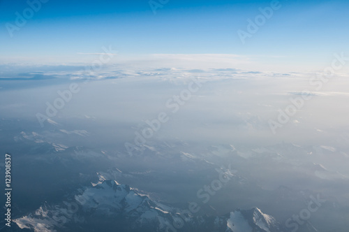 Aerial view from airplane flying above white abstract clouds and mountains ridge with copy space for background design