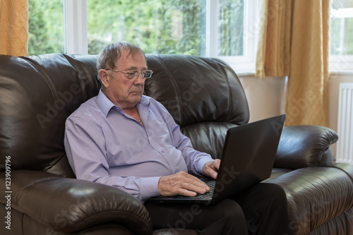 Old aged pensioner, man sat on sofa using a laptop