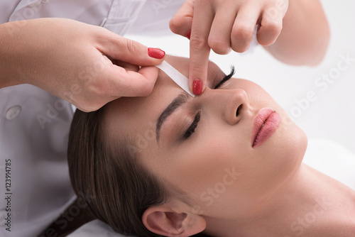 Young woman tweezing her eyebrows in beauty saloon