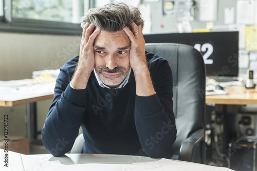 Mature man sitting in office with head in hands photo