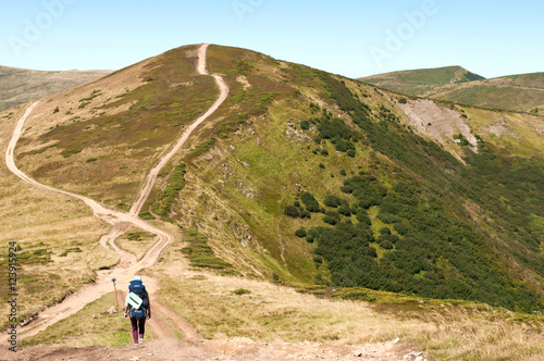 A girl with a backpack heading to a mountain hill