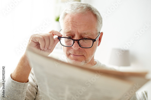senior man in glasses reading newspaper at home