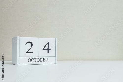 Closeup white wooden calendar with black 24 october word on blurred white wood desk and cream color wallpaper in room textured background with copy space , selective focus at the calendar