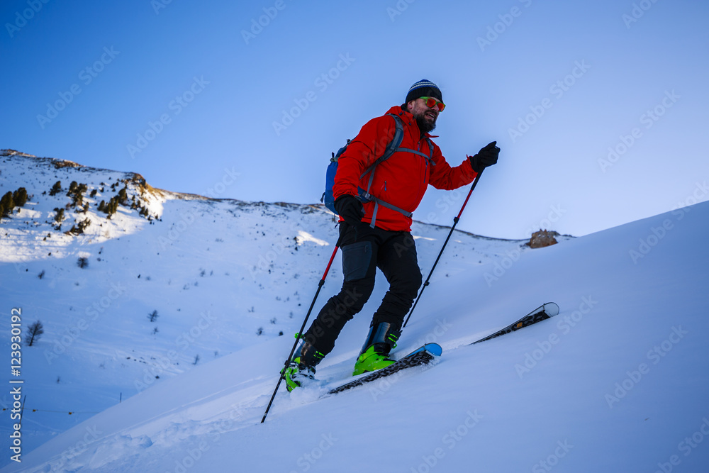 Ski touring man reaching the top at sunrise in Swiss Alps.