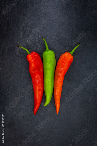 Two red and one green peppers on a gray slate