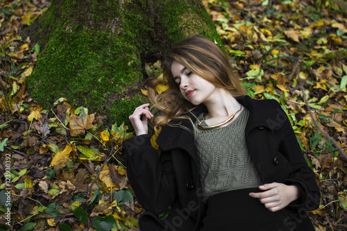 The girl lies on yellow leaves in autumn coat