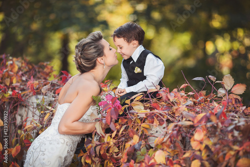 Wedding bride and child. Beautiful bride kisses small gentelman on the nose in the autumn park after wedding ceremony    photo