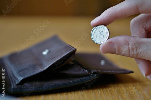 Male hand holding one coin from the United Arab Emirates (UAE dirham, AED) and withdrawing that from the brown leather wallet