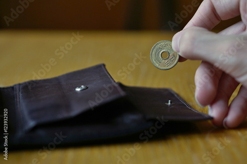 Male hand holding a bronze coin of five Yens (Japanese Yen, JPY) and withdrawing that from the brown leather wallet 