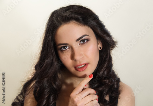 Charming European woman with brunette curly silky hair,expressive eyes,red nail polish,close up 