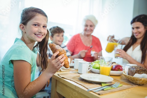 Smiling girl eating a croissant while having breakfast