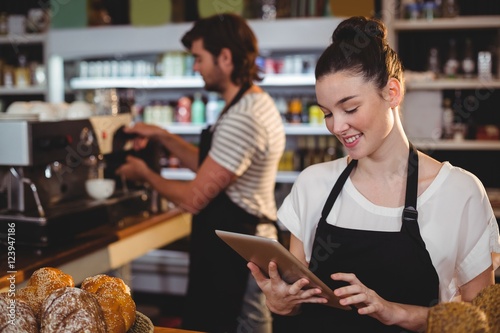 Smiling waitress standing at counter using digital tablet