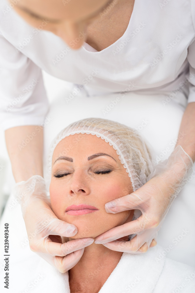Mature lady lying during facial examination at spa