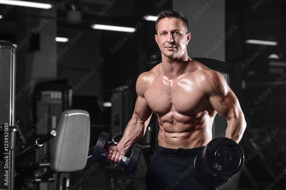 Handsome athletic fitness man posing and trains in the gym.