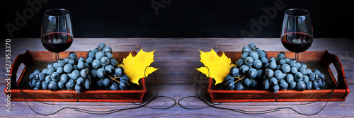 Canvastavla Red wine in wine glass and bunch of dark red grapes in a bowl on wooden board against black background