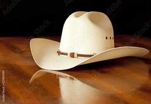 White straw cowboy hat with a hatband on a wooden table against dark background