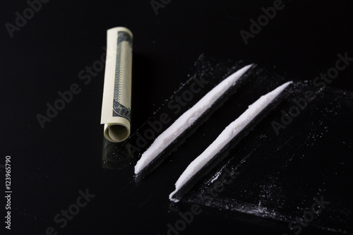 Rolled hundred dollars banknote and two lines of cocaine on blac