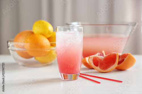 Glass of pink lemonade and grapefruits on white table
