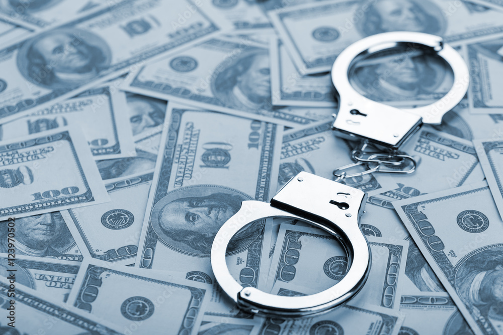 Pair of handcuffs closeup on dollar banknotes background Pair of handcuffs closeup on dollar banknotes background