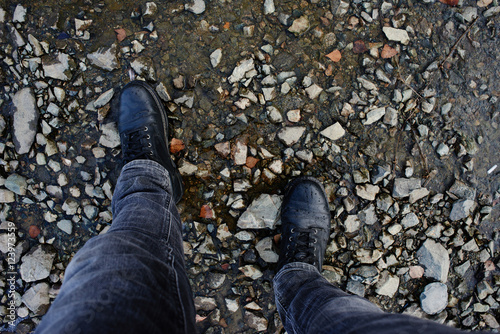 The view from the top, feet in jeans and leather shoes standing on the stony shore