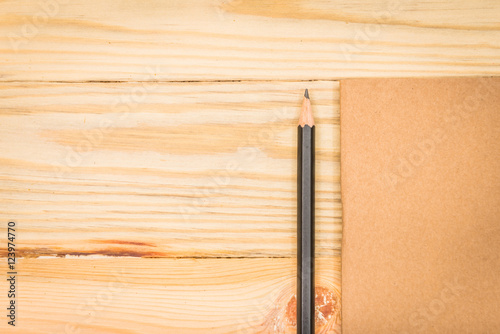 Brown note book with pencil on wood background