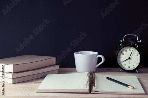 Notebook with pencil, cup of coffee,clock and books on table.