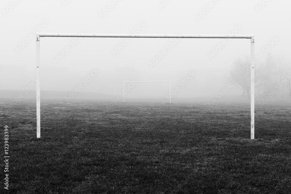Black and white image of soccer football goal posts in empty field pitch in winter fog