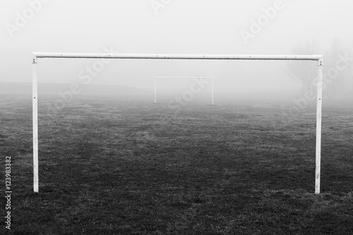 Black and white image of soccer football goal posts in empty field pitch in winter fog