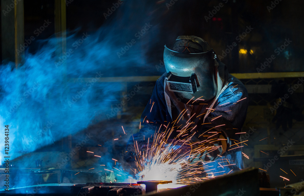 Worker with protective mask welding automotive part in factory Worker with protective mask welding automotive part in factory