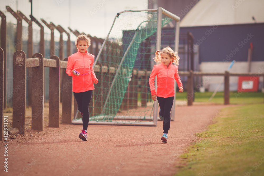 Two young girls running on athletic race track
